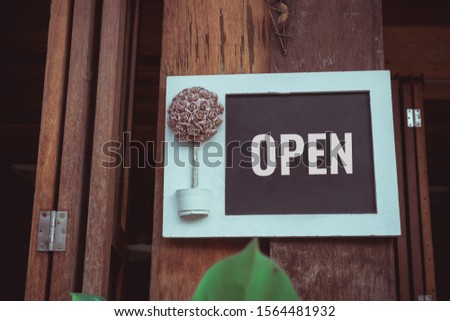 Open sign wooden , mock up board with paper flowers bouquet hanging on door at front of cafe or rent house with wood background. Business service