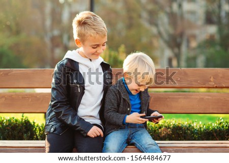 Sweet little boy playing video game on smartphone. Happy children playing online games outdoors. Funny blonde brothers having fun together. Happy family on a walk