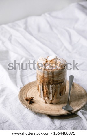 Hot chocolate or cocoa with marshmallow served in ceramic mug with saucer and spoon on white folded table cloth.