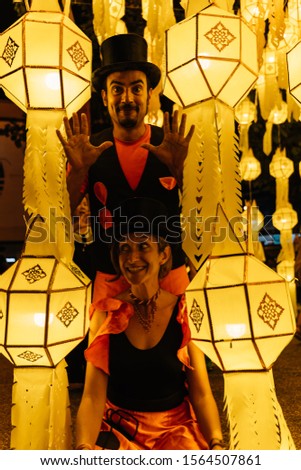 Stock vertical photo of a couple of tightrope walkers in disguise and wearing a black hat with a graceful expression surrounded by Chinese lanterns at night