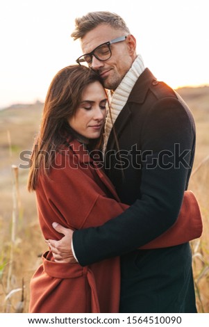Image of a pleased beautiful adult loving couple walking outdoors at the nature hugging.