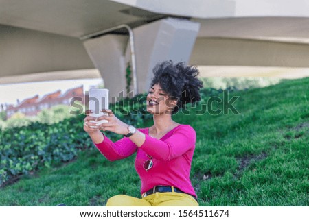 Afro hair racial woman takes a selfie photo of herself with her tablet. in the middle of a large outdoor park