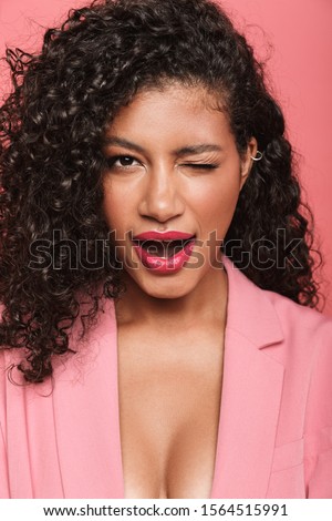 Portrait of a beautiful lovely young african woman wearing summer clothing standing isolated over pink background, winking