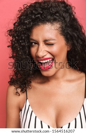 Portrait of a cheerful beautiful young african woman wearing summer clothing standing isolated over pink background, winking