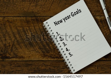 Table top view aerial image of 2020 new year business  goals & plans concept.Flat lay of essential object on brown wood.Text on notepad with black coffee and pen for accessories office desk backdrop