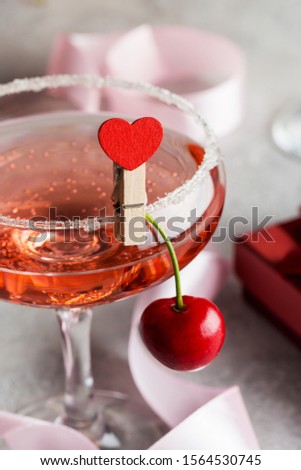 Champagne glass with pink wine on eve with gift box and red ribbon on gray background. Concept of holiday party's drink