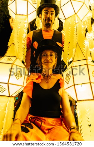 Stock vertical photo of a couple of tightrope walkers in disguise and wearing a black hat surrounded by Chinese lanterns at nigh. Lifestyle and nomad