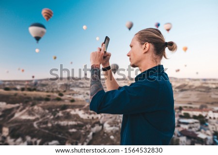 Man taking photo of beautiful landscape and balloons in Cappadocia with mobile camera, dreamy travel concept.