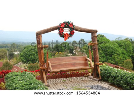 Wooden swing chair have Christmas wreath with metal Merry Christmas word on top with nature environment background