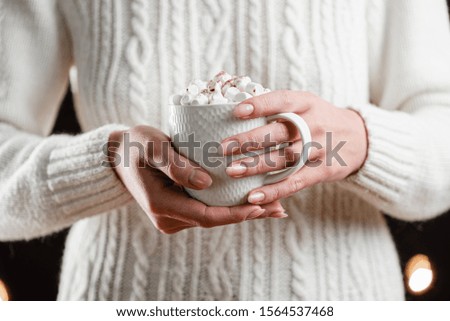 White cup of hot christmas cocoa with marshmallows in woman's hands. Close-up.