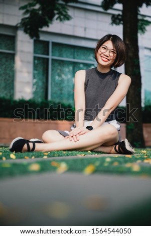Portrait of Asian young short hair beautiful woman wearing glasses and grey dress sit on the ground in the garden