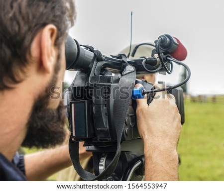 video camera, cameramanon green grass field background.photographer records the sunset in the background of meadow.Professional videographer on adventure vacation shooting camera on steadicam.