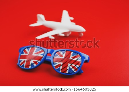 White airplane and sunglasses with the flag of the United Kingdom on a red background. Travel to England.