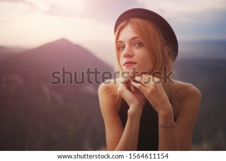 Close-up of a young Caucasian woman in a black dress and black hat on a sunset background high in the mountains of Bulgaria. Real grain scanned film.