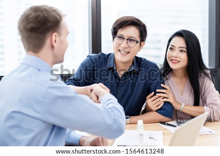 Couples asian made signing real estate leases, they have smilly and happy faces. They hand shake with realtors.
