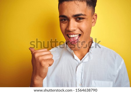 Young brazilian businessman wearing elegant shirt standing over isolated yellow background pointing and showing with thumb up to the side with happy face smiling