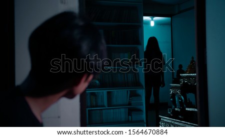 A man looking at scariest Thai lady ghost across the room staring at him.The lady ghost is completely in silhouette. Royalty-Free Stock Photo #1564670884