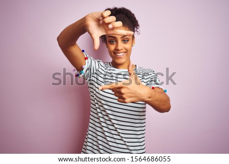 African american woman wearing navy striped t-shirt standing over isolated pink background smiling making frame with hands and fingers with happy face. Creativity and photography concept.