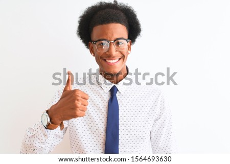 Young african american businessman wearing tie and glasses over isolated white background doing happy thumbs up gesture with hand. Approving expression looking at the camera showing success.