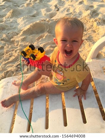 a child of European appearance, with blond hair and big eyes, covered in sand, sitting on a deck chair, holding a typewriter and screaming. relaxation on the beach of a paradise island, genuine emotio