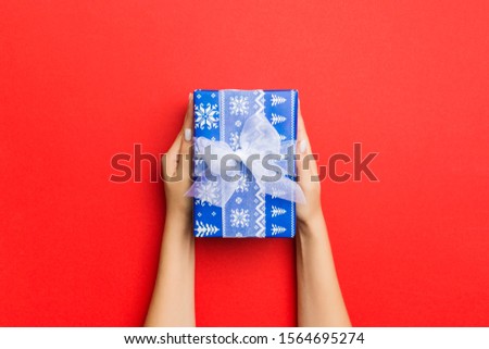 Female's hands holding striped gift box with colored ribbon on red background. Christmas concept or other holiday handmade present box, concept top view with copy space.