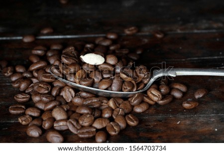 Pile of fresh coffee beans,overflowing off the spoon and topped with a white cocoa bean on an old wooden tray