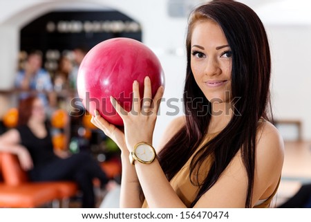 Portrait of beautiful young woman holding pink ball in bowling club