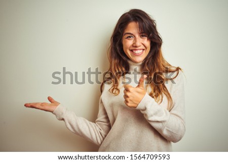 Young beautiful woman wearing winter sweater standing over white isolated background Showing palm hand and doing ok gesture with thumbs up, smiling happy and cheerful