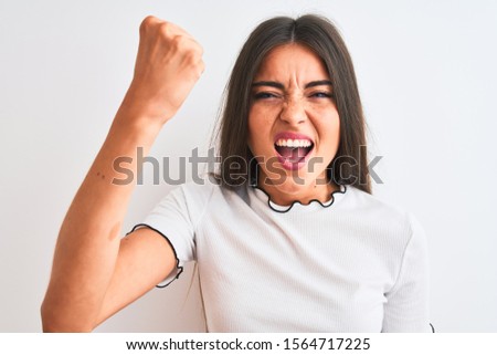 Young beautiful woman wearing casual t-shirt standing over isolated white background annoyed and frustrated shouting with anger, crazy and yelling with raised hand, anger concept