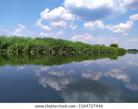 Sunny summer morning. Fluffy white clouds are reflected in the blue water of the river.