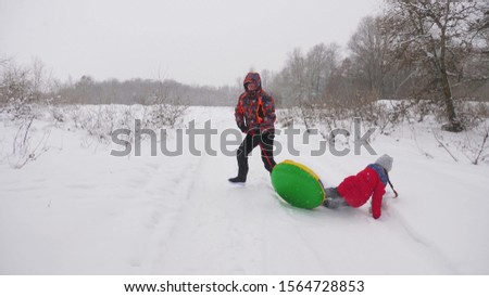 Happy dad sledges a child on a snowy road. Christmas Holidays. father plays with his daughter in a winter park. The concept of happy family. A teenager rides in Tubing