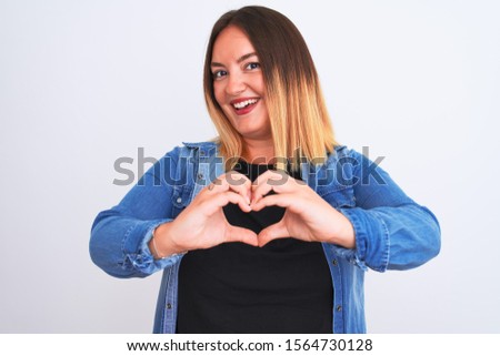 Young beautiful woman wearing denim shirt standing over isolated white background smiling in love showing heart symbol and shape with hands. Romantic concept.