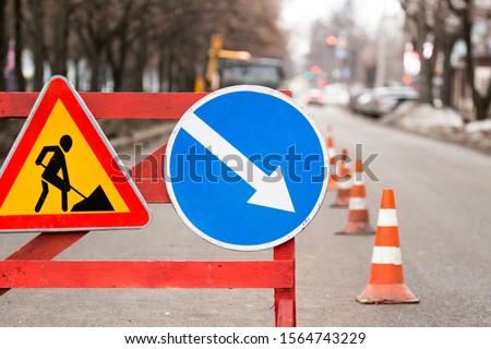 Under construction board sign on the closed road with arrow sign and traffic cone.