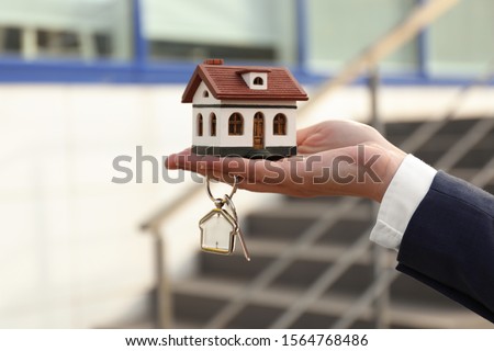 Real estate agent holding key and house model outdoors, closeup Royalty-Free Stock Photo #1564768486