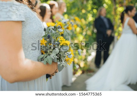Bridal party during outdoor wedding ceremony, focus on flowers.