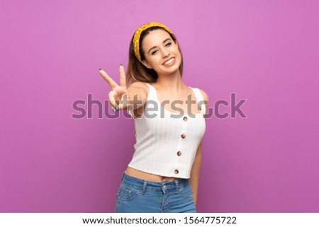Pretty young woman over isolated purple wall smiling and showing victory sign