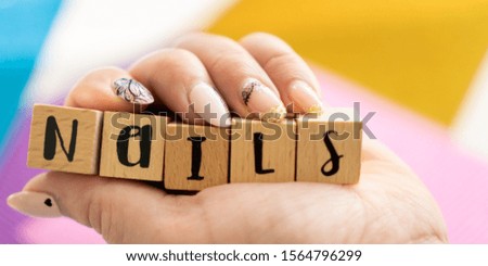 A female hand holding wooden cubes arranged in the word nails. Manicure of women's hands.