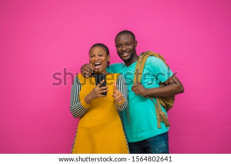 Handsome black man holding his phone standing close to a beautiful girl holding her phone giving thumbs up with a great smile on their faces