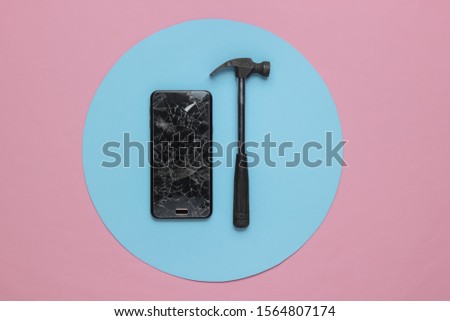 Smartphone with broken glass screen and hammer on blue pink background. Top view