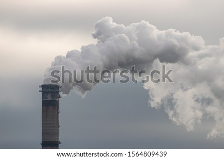 Smoke and steam produced off from the chimney against dark stormy sky Royalty-Free Stock Photo #1564809439