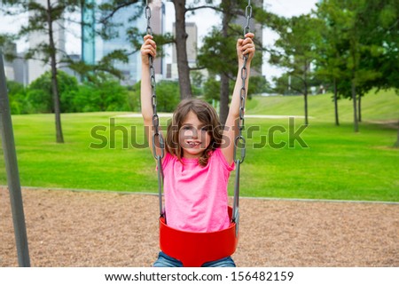 Brunette kid girl playing with swing on park with city skyline background
