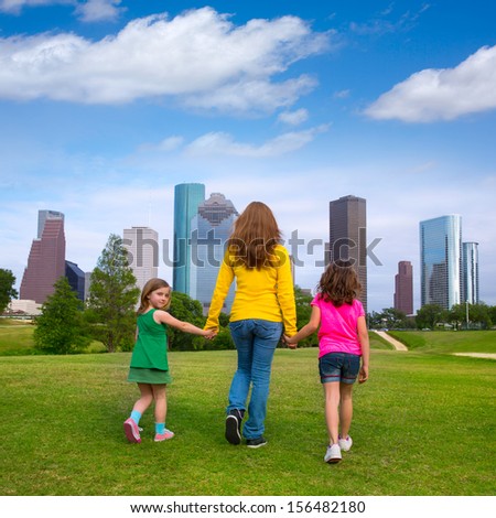 Mother and daughters walking holding hands on modern city skyline over park green lawn