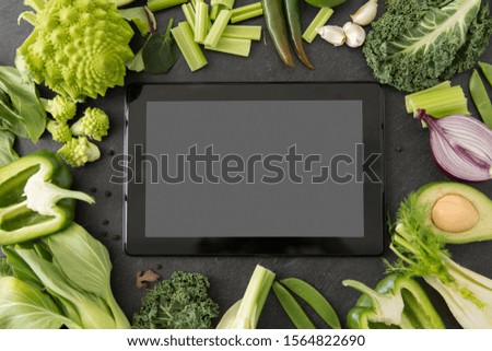 food, diet and healthy eating concept - close up of different green vegetables and tablet pc computer with blank screen on slate stone background