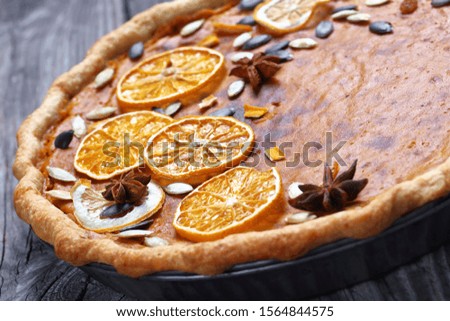close-up of sweet potato pie decorated with orange chips, pumpkin seeds and anise stars on a rustic wooden table, horizontal view from above,
