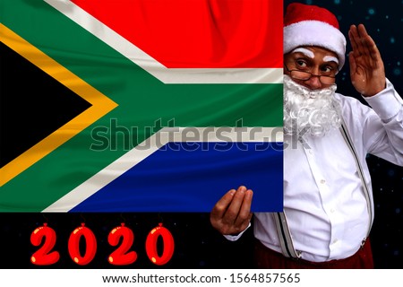 Santa Claus with a beard holds the beautiful colored national flag of the state of South Africa on fabric, concept of tourism, new year and christmas, economic and political prospects