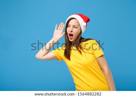 Curious young brunette woman Santa girl in Christmas hat posing isolated on blue background. Happy New Year 2020 celebration holiday concept. Mock up copy space. Try to hear you with hand near ear