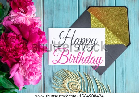 Happy birthday greeting card with peonies flowers on a wooden background with envelopes. Flat lay, top view.
