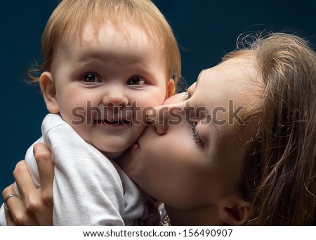 A beautiful young mother, or a nanny, or a foster mother, hugs and kisses the little girl, expressing love and affection for an orphan or for her own daughter, the child happily smiles at the camera.