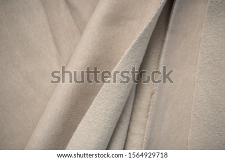 Woolen beige knitted fabric in soft folds. Texture as a background. Sewing pattern. Cut cotton piece.