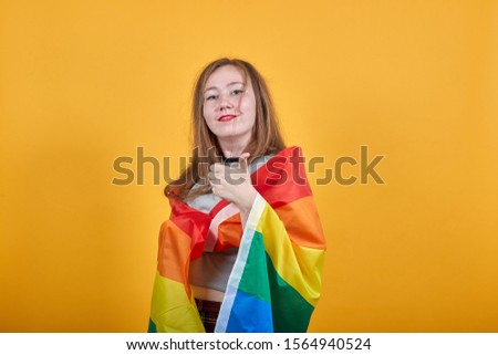 Pretty young girl over isolated orange wall wearing fashion clothes celebrating a victory in winner position, keeping fist up, covering LGBT flag